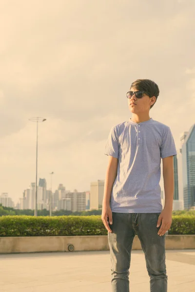 Mladý asijský dospívající chlapec nosí sluneční brýle při relaxaci v parku — Stock fotografie