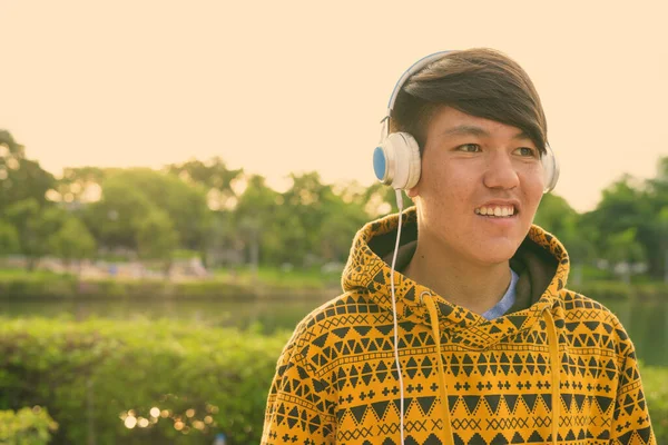 Νεαρό ασιατικό έφηβος φορώντας ακουστικά, ενώ χαλαρώνουν στο πάρκο — Φωτογραφία Αρχείου