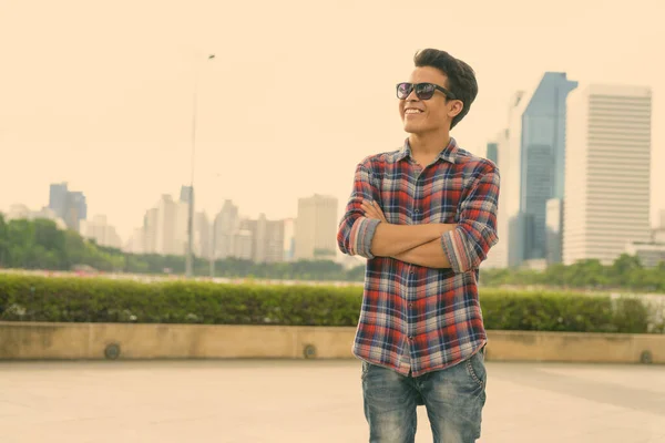 Fiatal ázsiai férfi napszemüveget visel, miközben a parkban pihen. — Stock Fotó