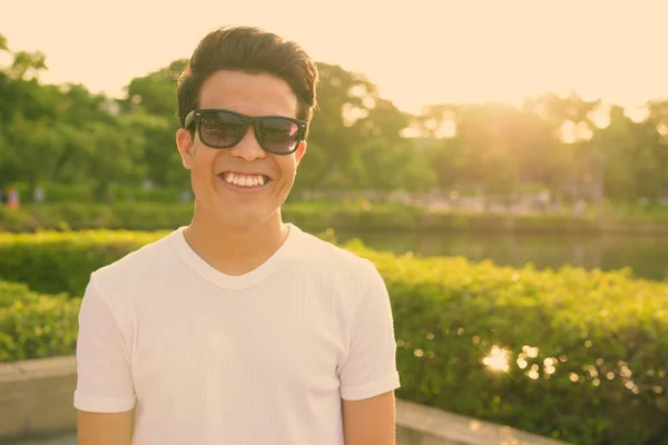 Молодий азіатський чоловік у сонцезахисних окулярах під час відпочинку в парку. — стокове фото