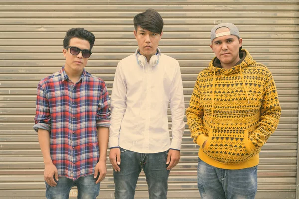 Троє молодих азіатських чоловіків стоять навпроти дверей складу на вулиці. — стокове фото