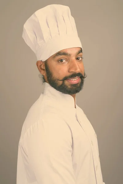 Young handsome Indian man chef against gray background