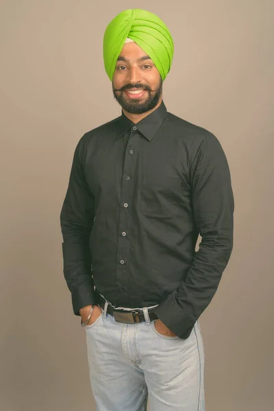 Молодой красивый индийский сикх бизнесмен в тюрбане на сером фоне — стоковое фото