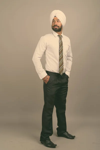 Young handsome Indian Sikh businessman wearing turban against gray background