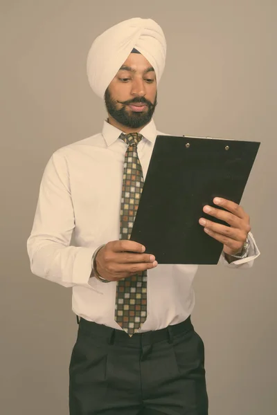 Young handsome Indian Sikh businessman wearing turban against gray background
