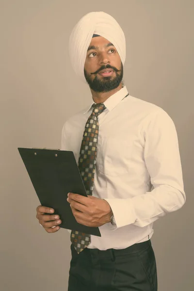 Young handsome Indian Sikh businessman wearing turban against gray background — Stock Photo, Image