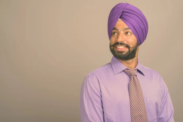 Young handsome Indian Sikh businessman wearing turban against gray background