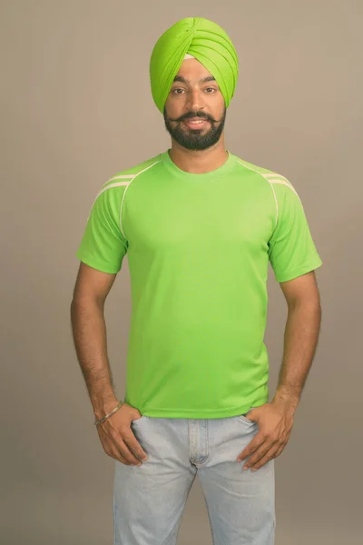 Joven hombre sikh indio guapo usando turbante contra fondo gris —  Fotos de Stock