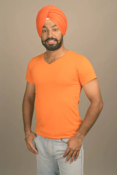 Joven hombre sikh indio guapo usando turbante contra fondo gris — Foto de Stock