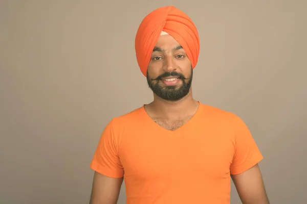 Mladý hezký indický sikh muž na sobě turban proti šedé pozadí — Stock fotografie