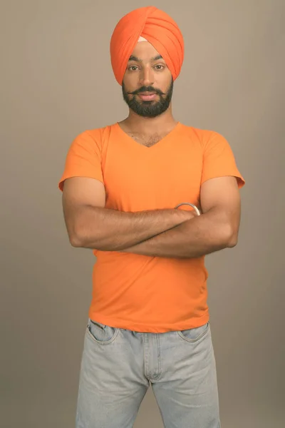 Jovem bonito indiana sikh homem vestindo turbante contra cinza fundo — Fotografia de Stock