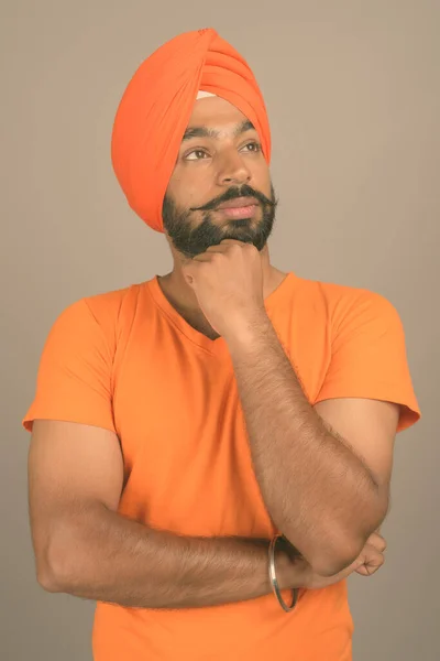 Jovem bonito indiana sikh homem vestindo turbante contra cinza fundo — Fotografia de Stock