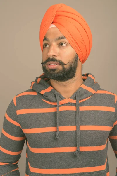 Jovem bonito indiana sikh homem vestindo turbante contra cinza fundo — Fotografia de Stock