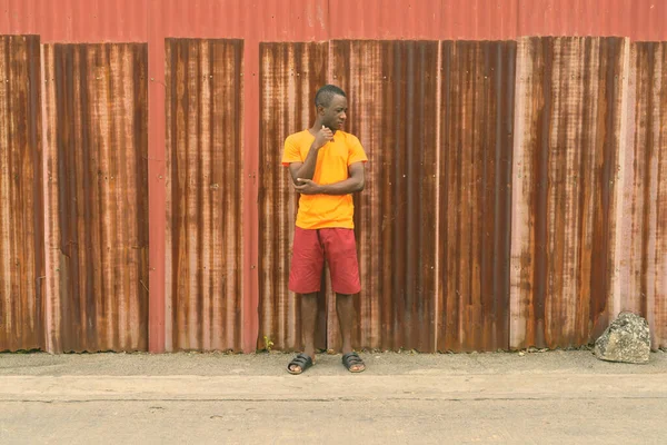Νέοι μαύροι Αφρικανοί σκέφτονται και κοιτάζουν κάτω ενώ στέκονται ενάντια στο παλιό σκουριασμένο τοίχο φύλλων — Φωτογραφία Αρχείου