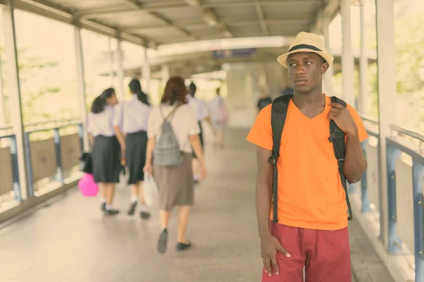 Νεαρός μαύρος Αφρικανός τουρίστας στέκεται και σκέφτεται στην πεζογέφυρα του σταθμού του μετρό στην Μπανγκόκ της Ταϊλάνδης — Φωτογραφία Αρχείου