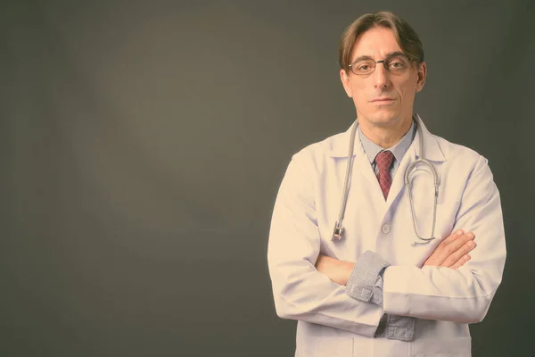 Mature handsome Italian man doctor against gray background — Stock Photo, Image