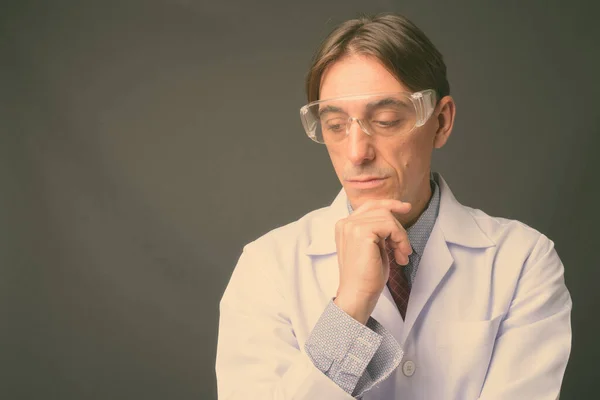 Maturo bello italiano uomo medico indossa occhiali protettivi contro sfondo grigio — Foto Stock