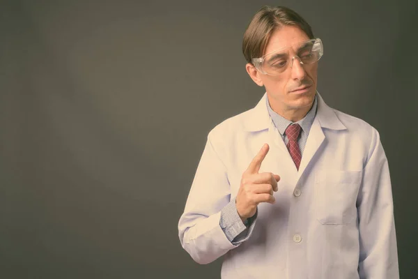 Reifer hübscher italienischer Arzt mit Schutzbrille vor grauem Hintergrund — Stockfoto