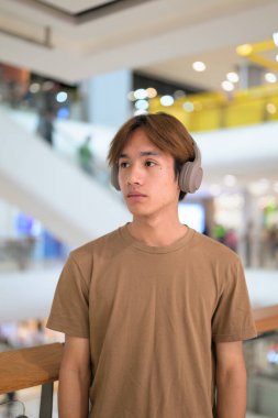 Kulaklıklı yakışıklı Asyalı genç Taylandlı modern yaşam tarzının tadını çıkarıyor müzik dinliyor.