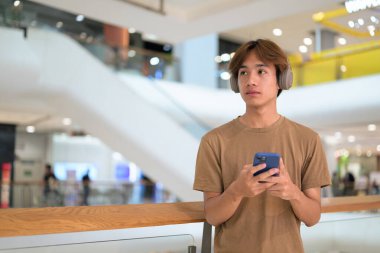 Boynuna kulaklık takmış 20 yaşındaki Taylandlı adam kafasında parlak bir alışveriş merkezi koridorunu, mesajlaşmayı, online alışverişi ve şehir yaşam tarzını araştırıyor..