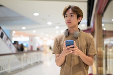 Boynuna kulaklık takmış 20 yaşındaki Taylandlı adam kafasında parlak bir alışveriş merkezi koridorunu, mesajlaşmayı, online alışverişi ve şehir yaşam tarzını araştırıyor..