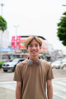 Kulaklıklı yakışıklı Asyalı genç Taylandlı yaz boyunca modern yaşam tarzının tadını çıkarıyor.