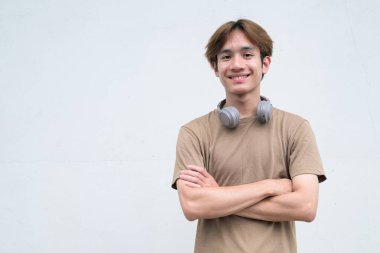 Kulaklıklı yakışıklı Asyalı genç Taylandlı beyaz arka planda modern hayat portresinin keyfini çıkarıyor.