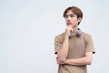 Kulaklıklı yakışıklı Asyalı genç Taylandlı beyaz arka planda modern hayat portresinin keyfini çıkarıyor.