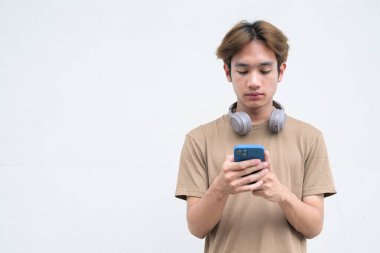 Kulaklıklı yakışıklı Asyalı genç Taylandlı beyaz arka planda modern hayat portresinin keyfini çıkarıyor.