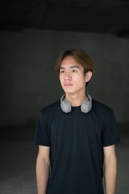 Siyah tişört giyen Taylandlı genç bir adam, gri beton duvarlar, modern yaşam tarzı, kentsel moda ve mimari anlayışına sahip, minimal barbar tarzı bir inşaat alanında poz veriyor.