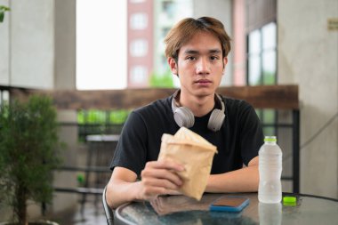 Mutlu Asyalı genç Taylandlı öğrenci öğle yemeği için dışarıda sandviç yiyor.