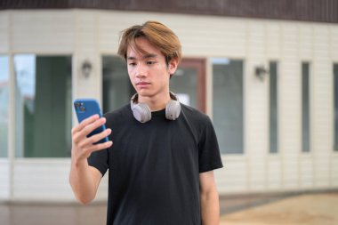 Açık havada telefon kullanan Taylandlı genç bir adamın portresi. Çeşitli kavramlar ve kullanımlar için kendine güvenen, rahat ve otantik görünüm