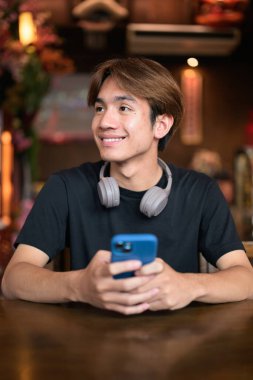 Geleneksel Çin tarzı çay restoranında telefonu sıradan tarzda kullanan Taylandlı genç bir adamın portresi. Çeşitli kavramlar ve kullanımlar için kendine güvenen, rahat ve otantik görünüm