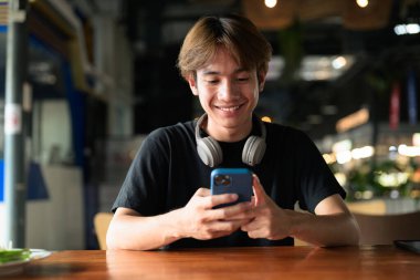 Gündüz otururken cep telefonu kullanan Taylandlı genç bir adamın portresi. Çeşitli kavramlar ve kullanımlar için kendine güvenen, rahat ve otantik görünüm