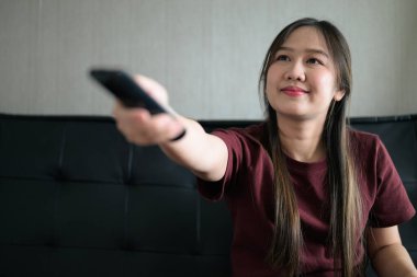 Genç Taylandlı kadın kanepede oturup evde televizyon izliyor. Modern eğlence, duygusal tepkiler ve rahatlama içeren sıradan bir ortamda hayat tarzı portresi..