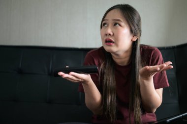 Genç Taylandlı kadın evde televizyon seyrediyor. Omuz silkerken stresli ve sıkkın görünüyor.