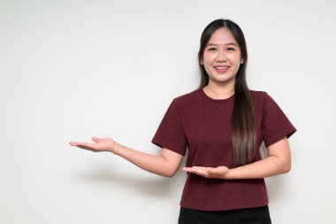 Genç Asyalı bir kadının stüdyo portresi beyaz arka plana karşı günlük tişört giyerek bir şeyler sunuyor.