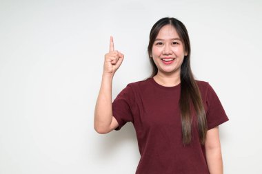 Genç, şirin Asyalı bir kadının, beyaz arka planı işaret eden, günlük tişört giyen bir stüdyo fotoğrafı.