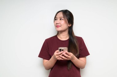 Genç, şirin Asyalı bir kadının beyaz arka planda günlük tişört giyerken cep telefonu kullanmasının stüdyo portresi.