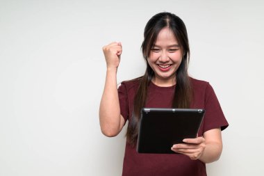 Beyaz arka planda, sıradan tişörtler giyen ve dijital tablet bilgisayar kullanan genç, sevimli Asyalı bir kadının stüdyo portresi.