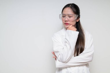 Beyaz arka planda güvenlik gözlüğü takan, laboratuvar önlüklü Asyalı sağlık görevlisi kadın portresi.