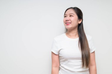 Sıradan beyaz tişört giyerek sade arka planda düşünen Asyalı genç bir kadının stüdyo portresi