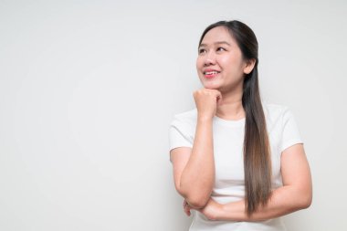 Sıradan beyaz tişört giyerek arka planda düşünen ve planlayan Asyalı genç bir kadının stüdyo portresi.