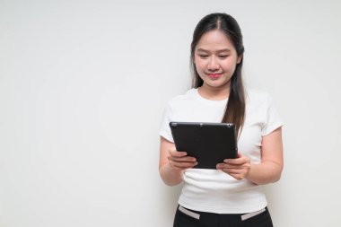 Sade beyaz tişört giyen ve dijital tablet bilgisayar kullanan Asyalı genç bir kadının stüdyo portresi.