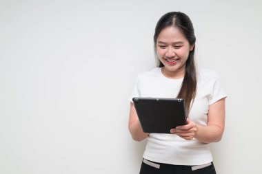 Sade beyaz tişört giyen ve dijital tablet bilgisayar kullanan Asyalı genç bir kadının stüdyo portresi.