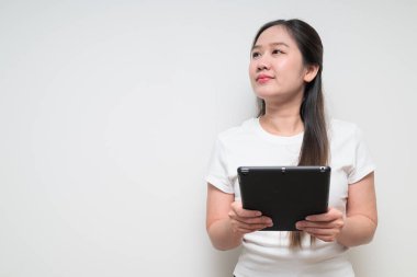 Sade beyaz tişört giyen ve dijital tablet bilgisayar kullanan Asyalı genç bir kadının stüdyo portresi.