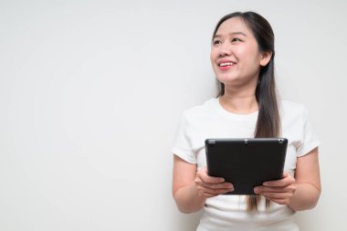 Sade beyaz tişört giyen ve dijital tablet bilgisayar kullanan Asyalı genç bir kadının stüdyo portresi.