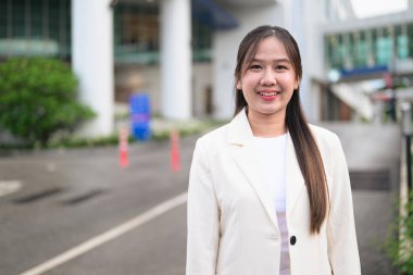 Güneydoğu Asyalı iş kadınının portresi şehir sokaklarında iş kıyafetleri içinde ve gülümserken kendinden emin görünüyor.