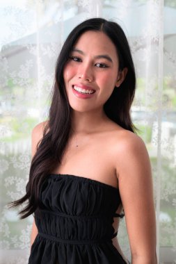 Genç ve güzel Asyalı bir kadının portresi gülümsüyor ve kapalı alanda kameraya bakıyor.