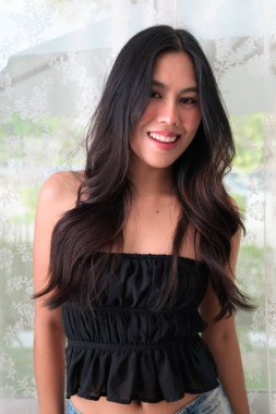 Genç ve güzel Asyalı bir kadının portresi gülümsüyor ve kapalı alanda kameraya bakıyor.